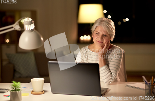 Image of senior woman with laptop at home in evening