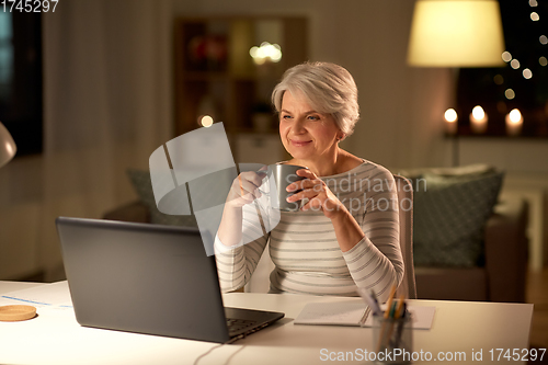 Image of senior woman with laptop drinking coffee at home