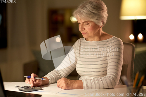 Image of old woman counting on calculator at home at night