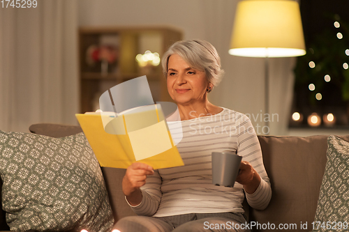 Image of senior woman reading book and drinking tea at home