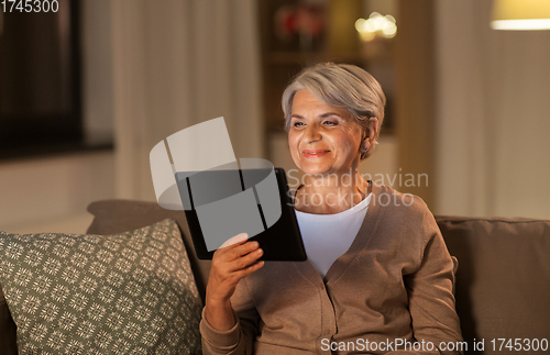 Image of happy senior woman with tablet pc at home at night