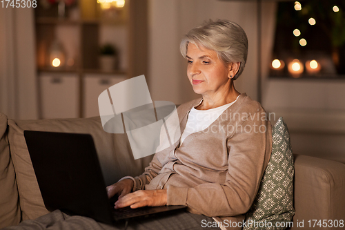 Image of happy senior woman with laptop at home at night
