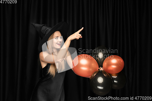 Image of Young woman in hat as a witch on black background