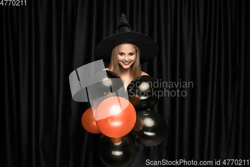 Image of Young woman in hat as a witch on black background