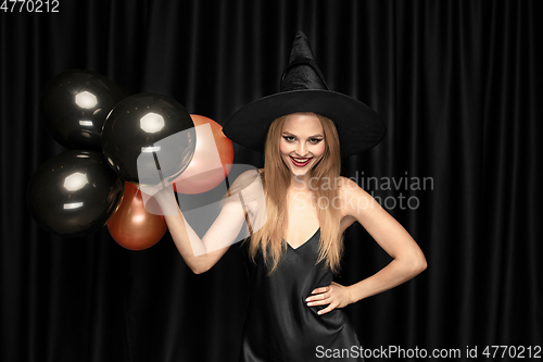 Image of Young woman in hat as a witch on black background