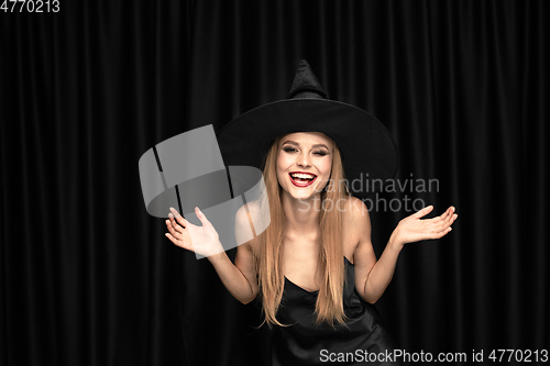 Image of Young woman in hat as a witch on black background