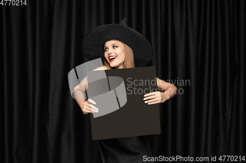 Image of Young woman in hat as a witch on black background