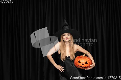 Image of Young woman in hat as a witch on black background