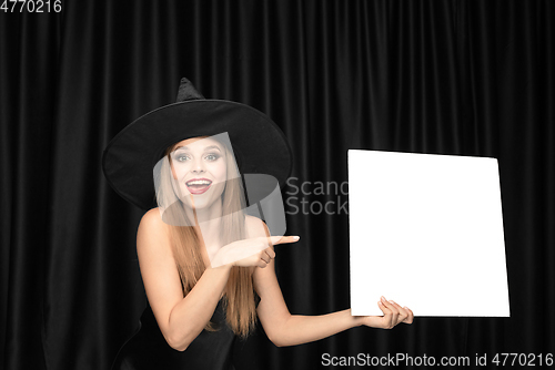 Image of Young woman in hat as a witch on black background