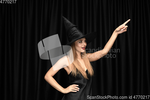 Image of Young woman in hat as a witch on black background