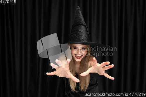 Image of Young woman in hat as a witch on black background