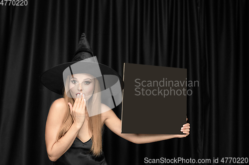 Image of Young woman in hat as a witch on black background