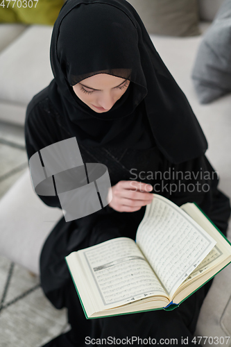 Image of Portrait of young muslim woman reading Quran in modern home