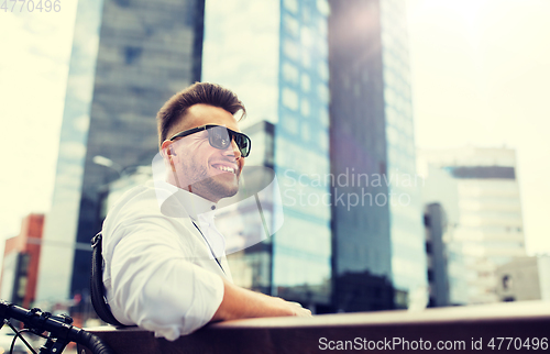 Image of happy young man with bicycle sitting on city bench