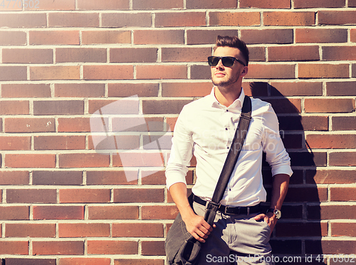 Image of young man in sunglasses with bag over brickwall