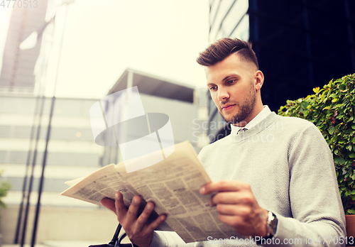 Image of man reading newspaper on city street bench