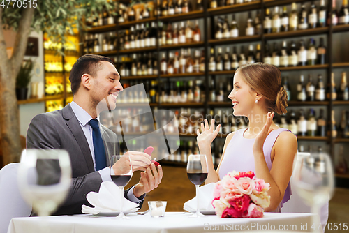 Image of man making proposal to happy woman at restaurant