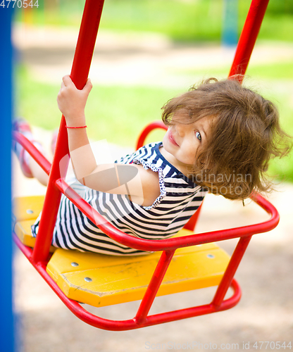 Image of Young happy girl is swinging in playground