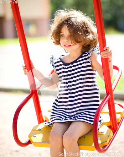 Image of Young happy girl is swinging in playground