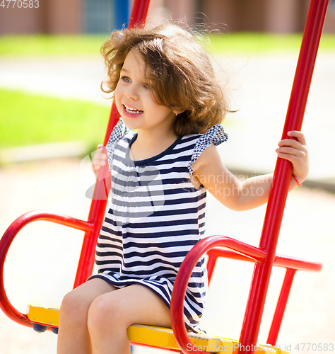 Image of Young happy girl is swinging in playground