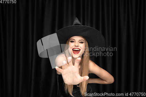 Image of Young woman in hat as a witch on black background