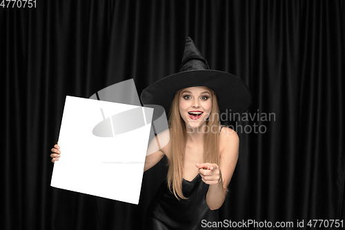 Image of Young woman in hat as a witch on black background