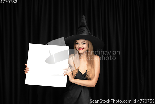 Image of Young woman in hat as a witch on black background