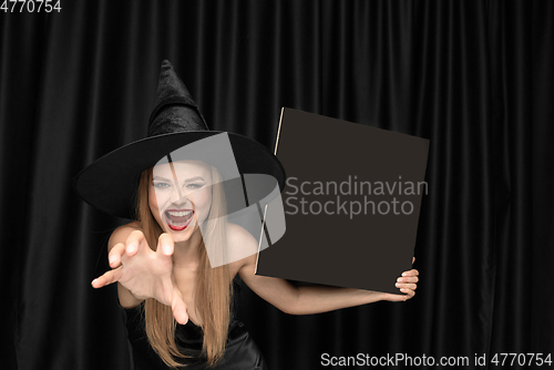Image of Young woman in hat as a witch on black background