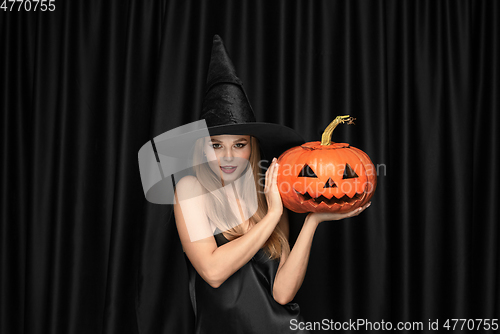 Image of Young woman in hat as a witch on black background
