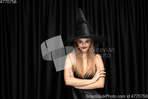 Image of Young woman in hat as a witch on black background