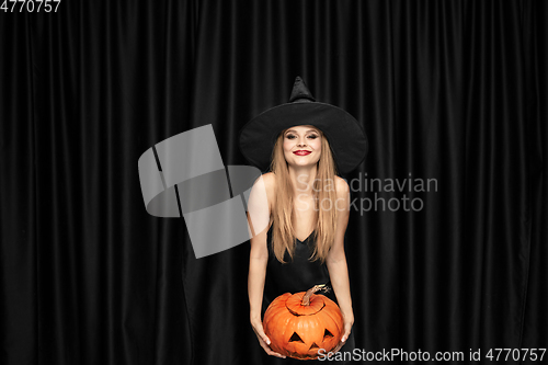 Image of Young woman in hat as a witch on black background