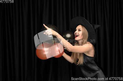 Image of Young woman in hat as a witch on black background