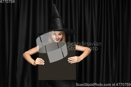 Image of Young woman in hat as a witch on black background