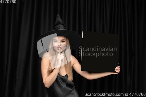 Image of Young woman in hat as a witch on black background