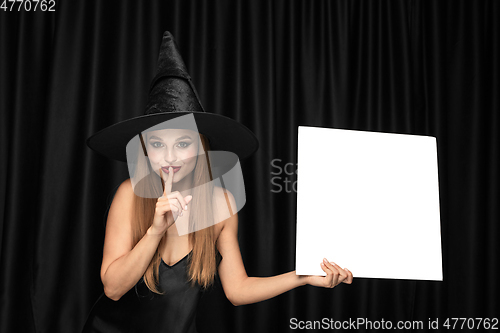 Image of Young woman in hat as a witch on black background