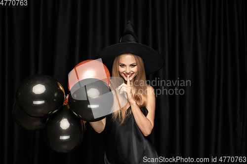 Image of Young woman in hat as a witch on black background