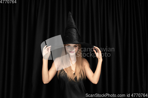 Image of Young woman in hat as a witch on black background