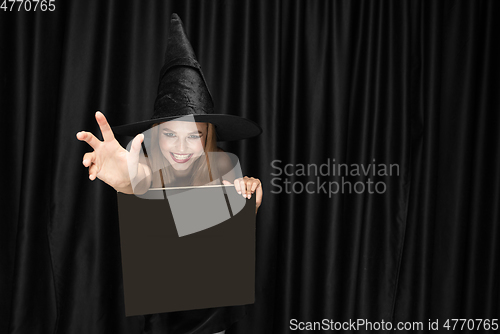 Image of Young woman in hat as a witch on black background