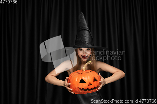 Image of Young woman in hat as a witch on black background