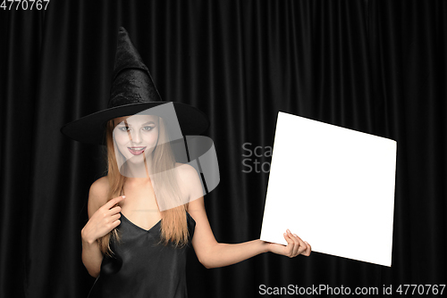 Image of Young woman in hat as a witch on black background