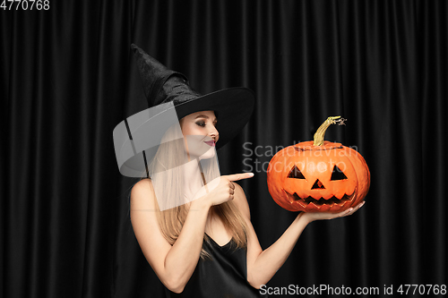 Image of Young woman in hat as a witch on black background