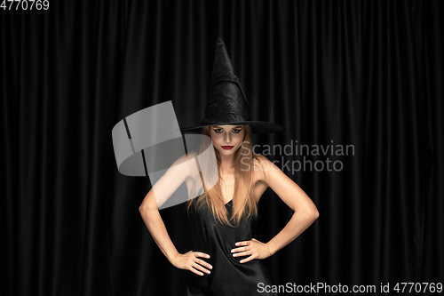 Image of Young woman in hat as a witch on black background