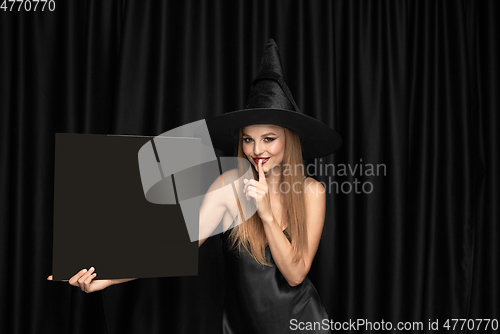 Image of Young woman in hat as a witch on black background