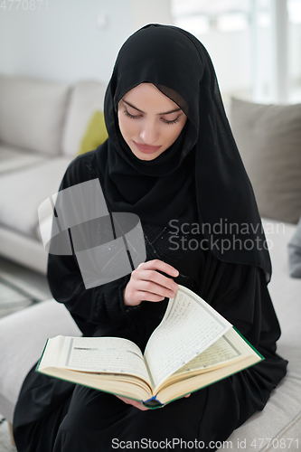 Image of Portrait of young muslim woman reading Quran in modern home