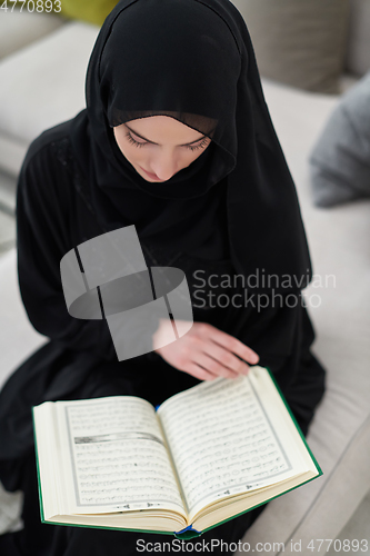 Image of Portrait of young muslim woman reading Quran in modern home