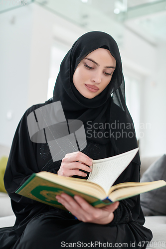 Image of Portrait of young muslim woman reading Quran in modern home