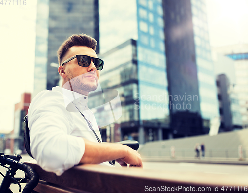 Image of happy young man with bicycle sitting on city bench