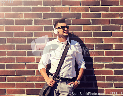 Image of young man in headphones with bag over brickwall