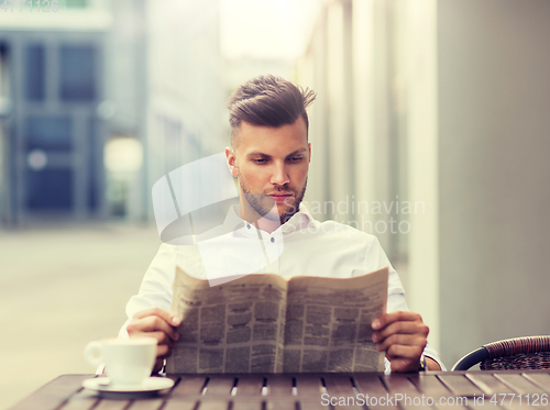 Image of smiling man reading newspaper at city street cafe