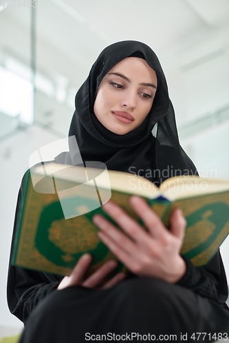 Image of Portrait of young muslim woman reading Quran in modern home